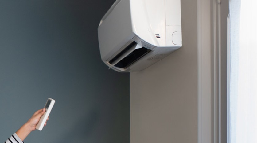 main avec une telecommande dirgée vers un split dans une maison